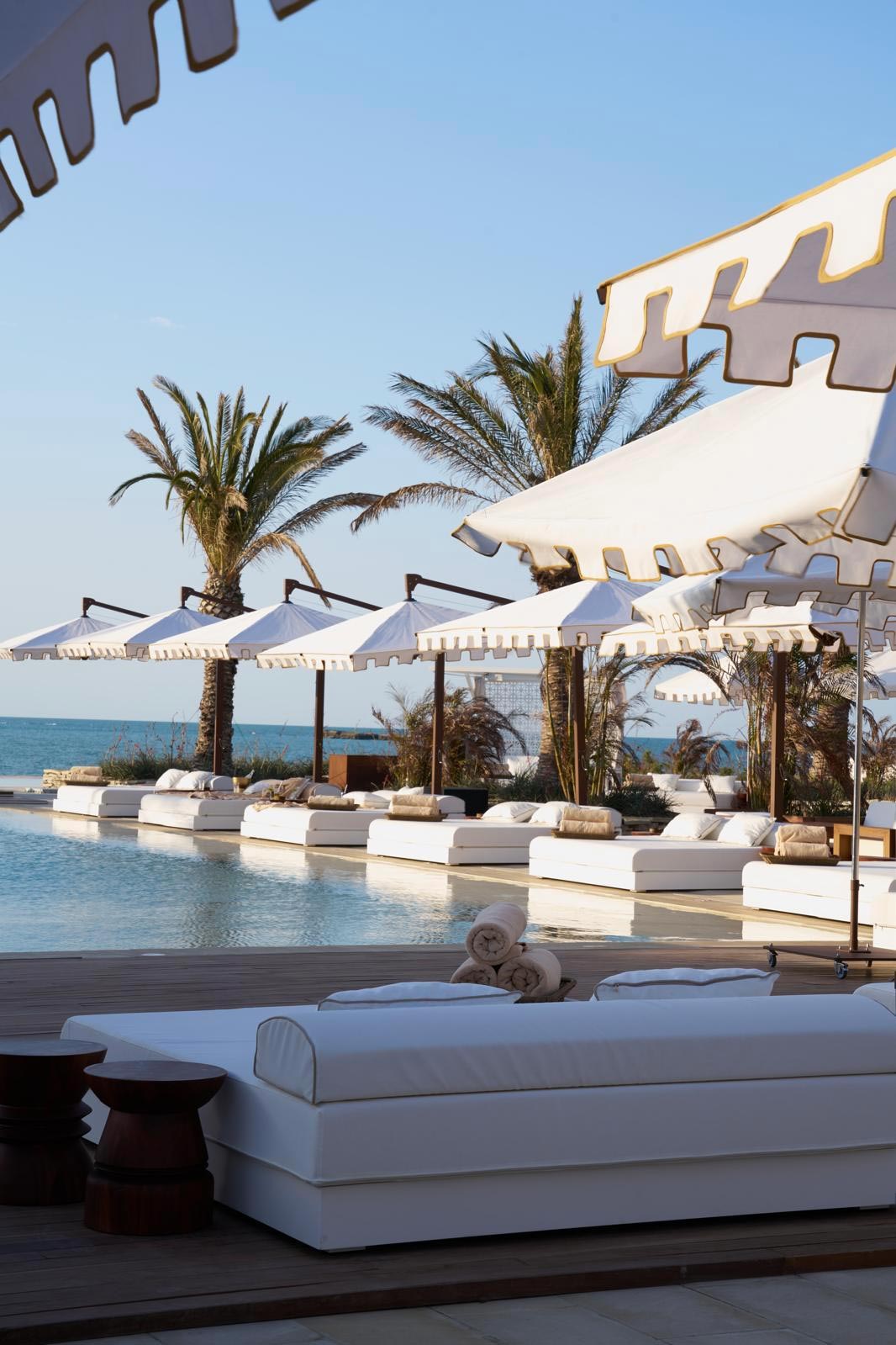 Lits de piscine et parasols blancs haut de gamme sur une terrasse d'hôtel par Mousses Étoiles.