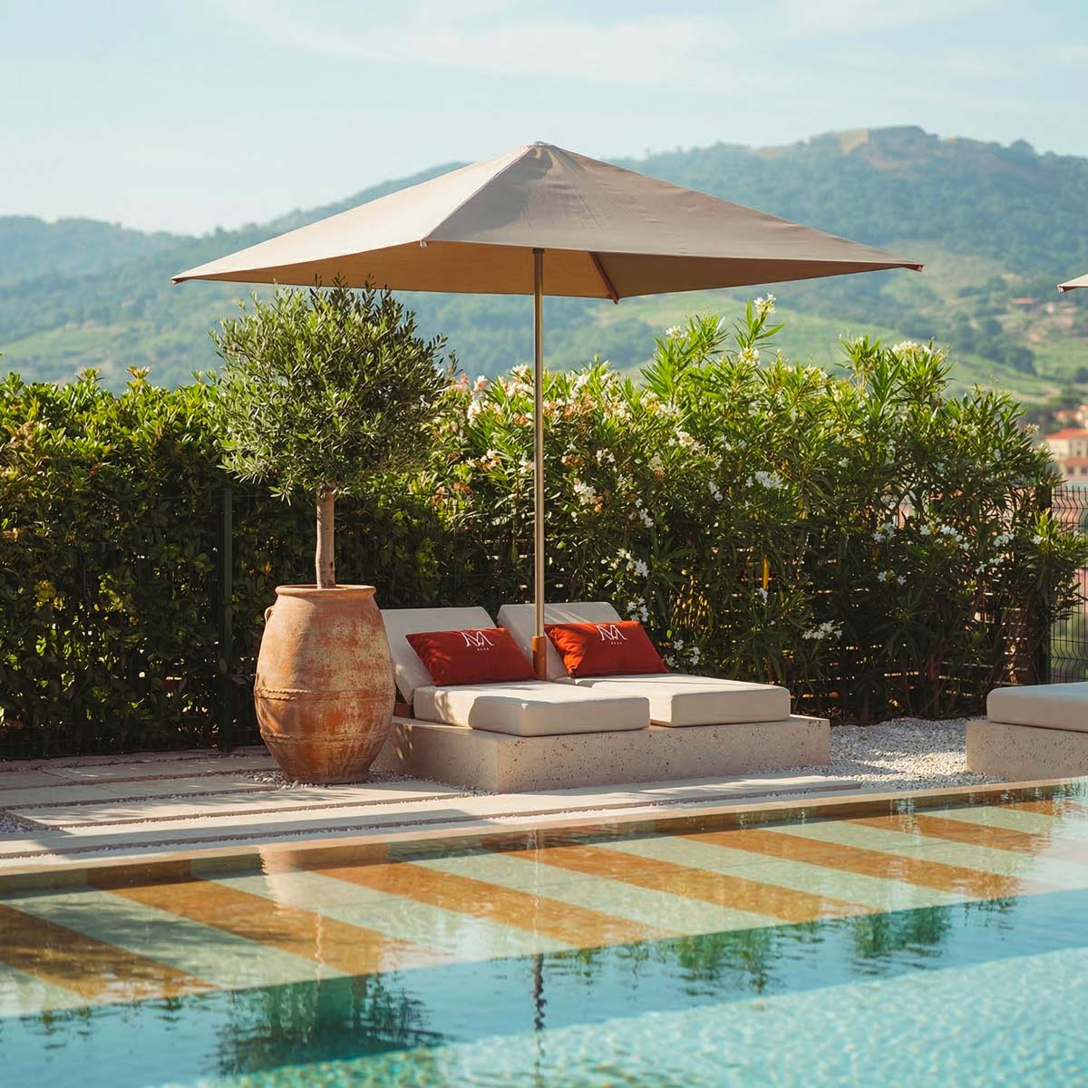 Parasol de luxe made in France ombrageant des bains de soleil avec coussins Mousses Étoiles au bord d'une piscine.